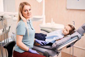 Adorable kid lying in dental chair beside female dental assistant.