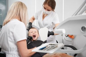 Young boy sitting in a dentist chair with a dentist and dental assistant looking at his teeth.