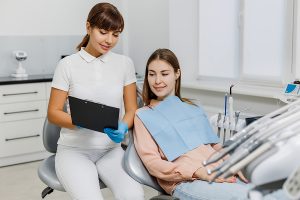 Friendly dental assistant with tablet explaining treatment to patient during teeth examination.