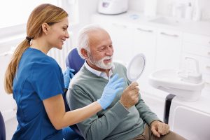 Senior Man Looking At The Mirror And Smiling After Checkup At Dentist