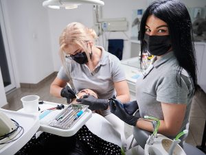 Dental assistant wearing gray scrubs standing in a treatment room with a dentist who is looking at a patient's teeth.