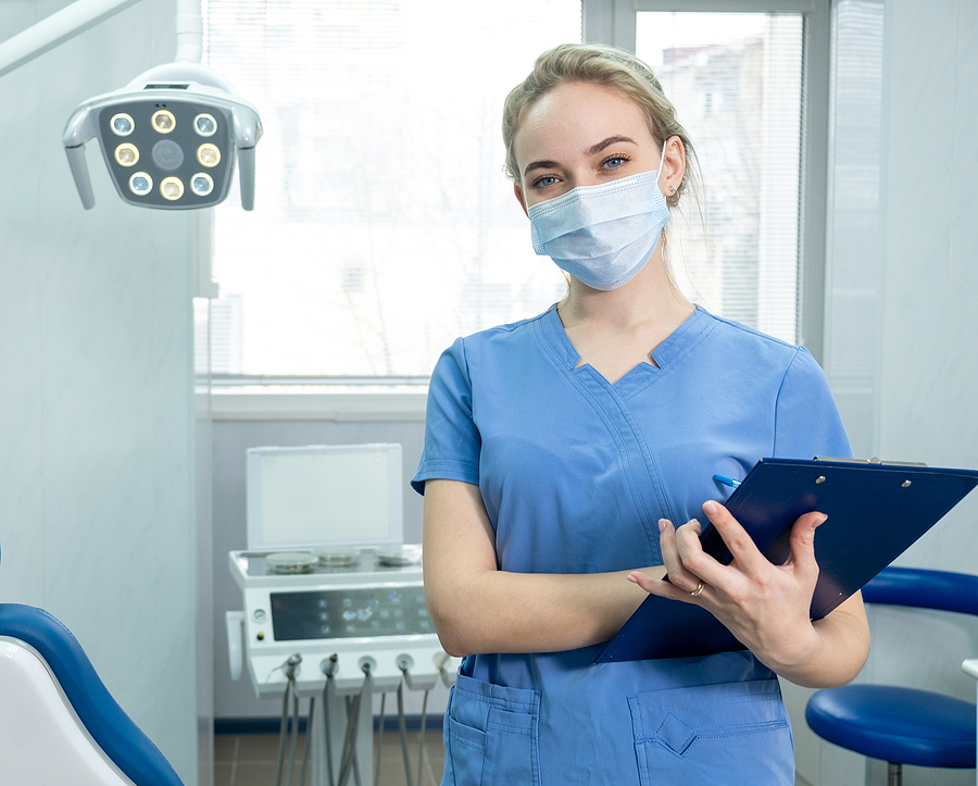 Female dental assistant wearing a mask holding a clip board in dental office