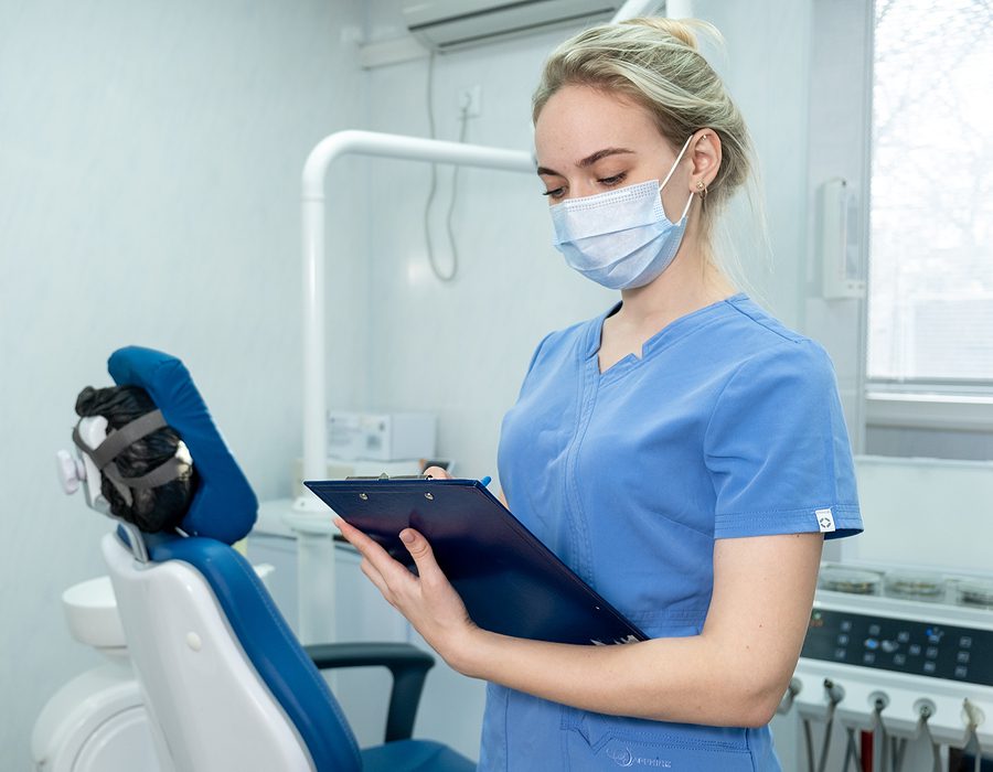 Female dental assistant wearing a mask and writing on a clip board in a dental office