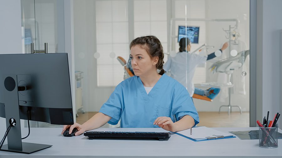 dental assistant sitting at desk logging patient information on a computer