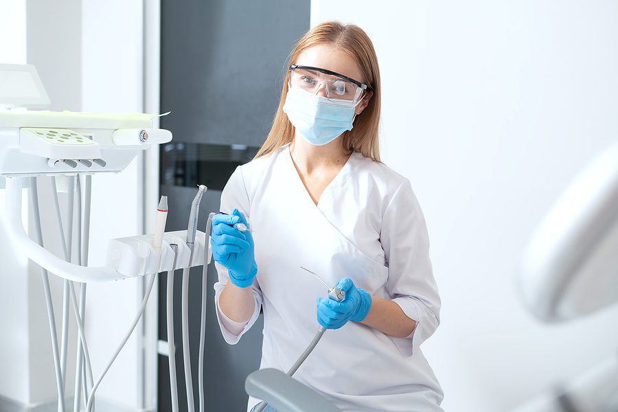 Dental assistant wearing gloves, goggles, and a mask holding dental equipment