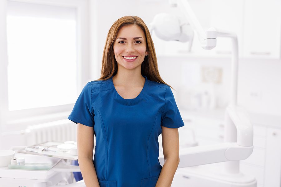 Dental assistant smiling while standing in a patient treatment room.