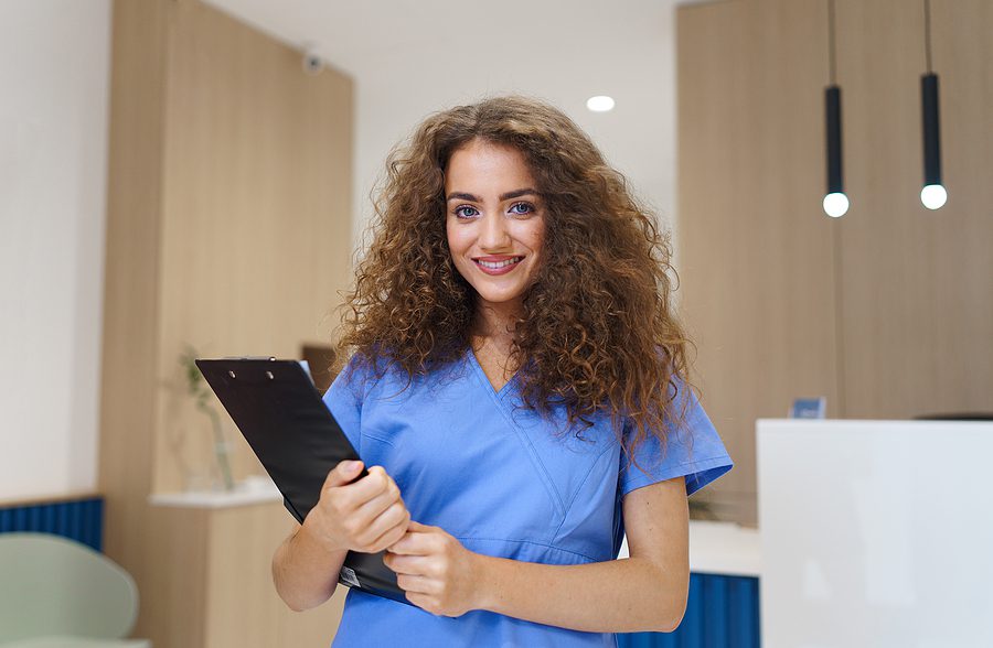 portrait of happy female dental office assistant with brown curly hair holding a clip board