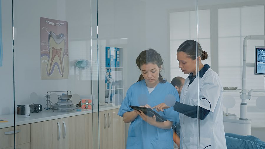 dental assistant and dentist consulting behind glass doors in dental office