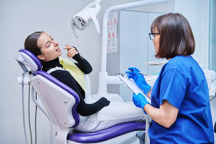 dental assistant writing information on patients chart as she points to an area in her mouth that hurts