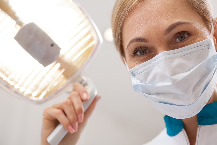 Smiling dental assistant holding treatment lamp.