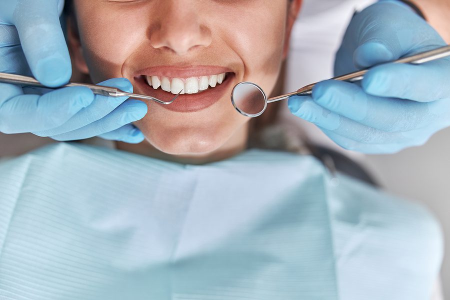 Cheerful positive dentist and client in dentistry. Female patient at dental procedure, doctor using dental instruments in modern dental clinic, close up.