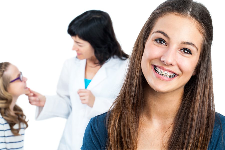 Close up portrait of Teen girl with dental braces and dentist with patient in background.Isolated on white. 