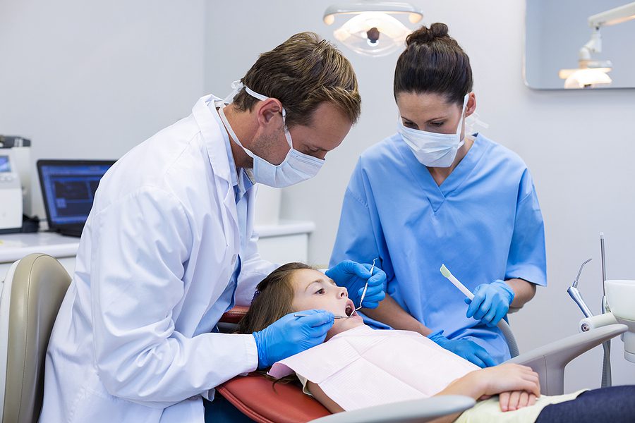 Dentist and dental assistant examining a young patient with tools in dental clinic
