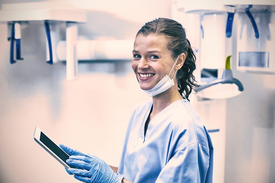 Dental assisting student smiling while wearing blue scrubs and holding a tablet