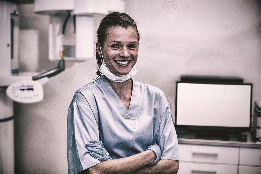 Smiling dental assistant standing with arms crossed in dental clinic. 