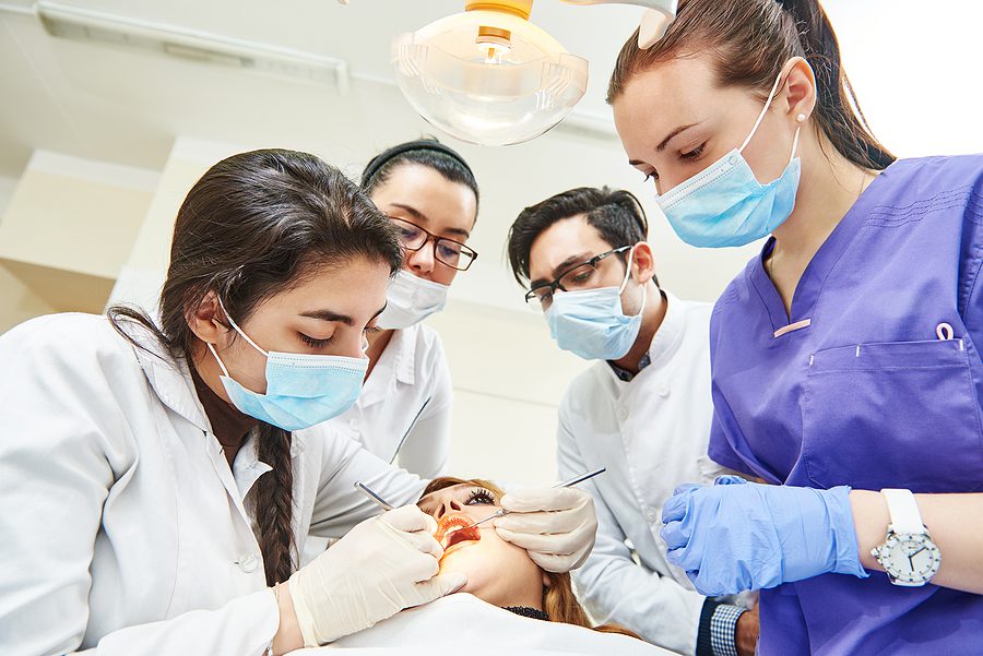 Dental assistant in purple scrubs learning a procedure with a group of dentists. 