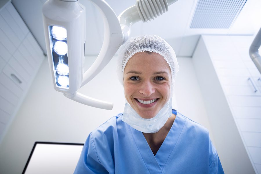 Dental assistant smiling at camera beside light in the dental clinic. 