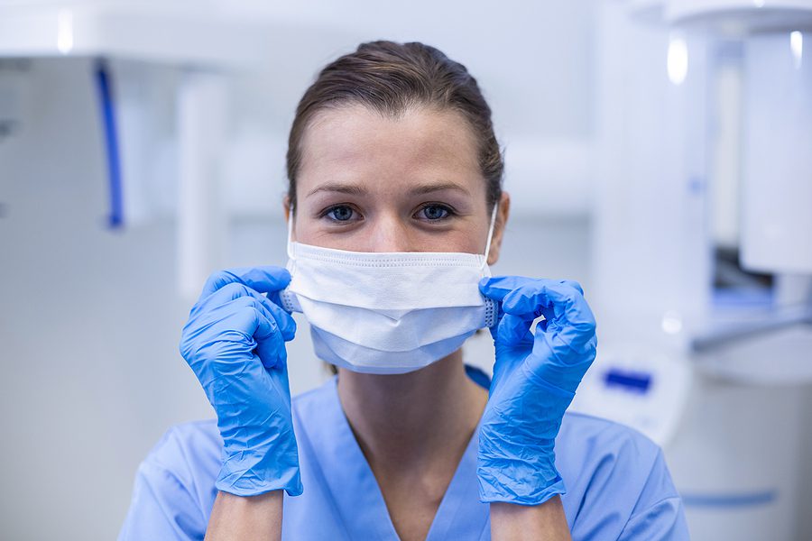 Close up of a female dental assistant wearing a surgical mask and blue gloves. 