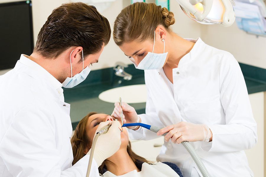 Close up of a male dentist and female dental assistant providing treatment to a patient. 