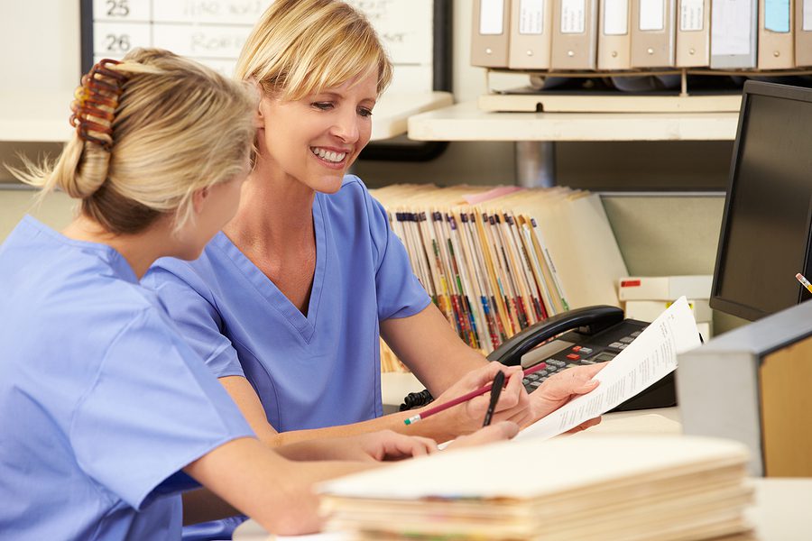 Two female dental office employees wearing scrubs, working at the front desk. 