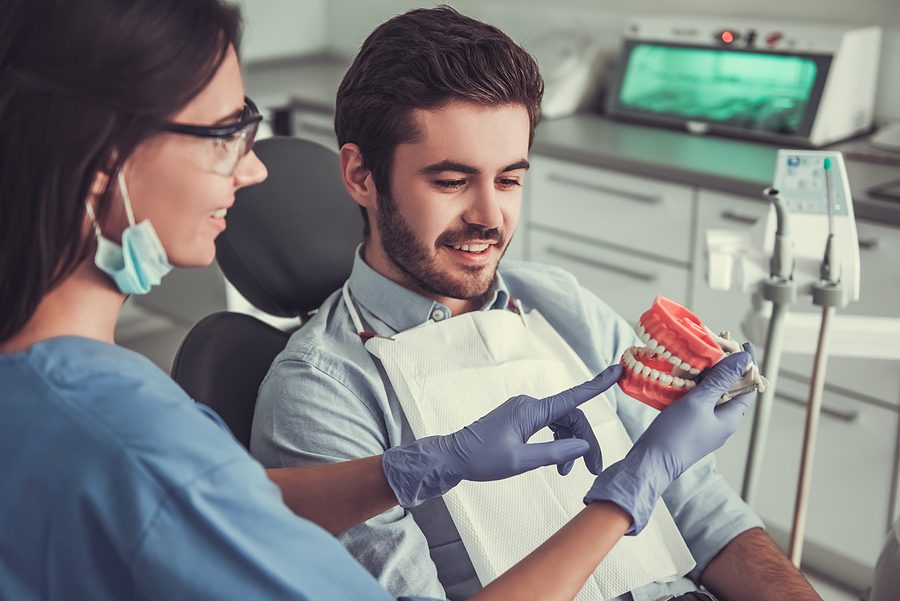 Female dental assistant is educating male patient about dental issue using a dental mold. 