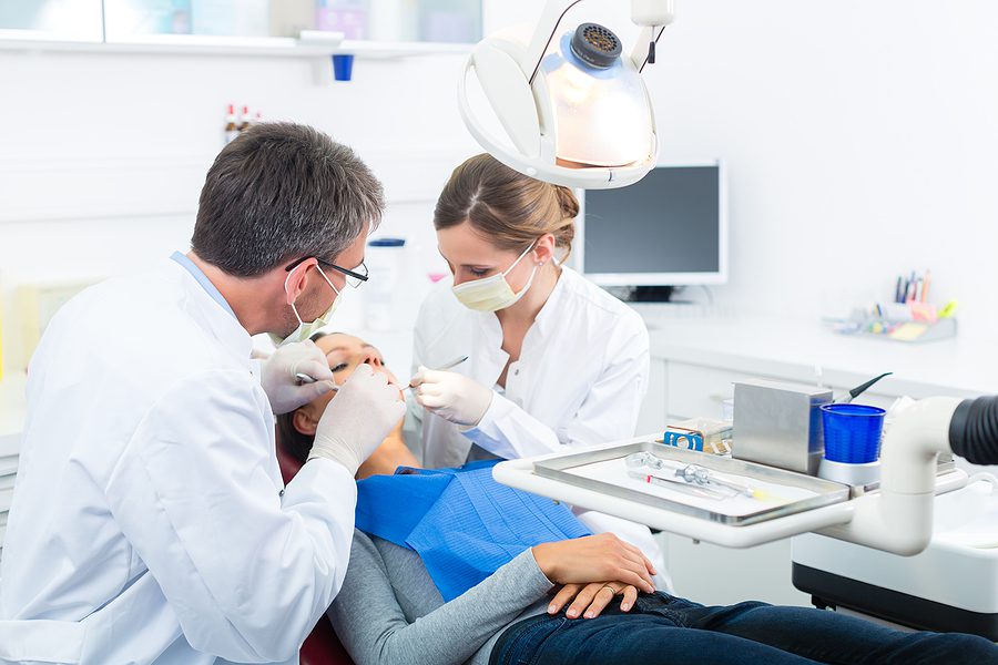 Male dentist and female dental assistant working in a dental treatment, wearing masks and gloves. 