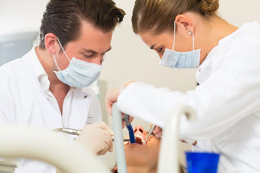 Female patient with dentist and dental assistant, performing a dental treatment. 