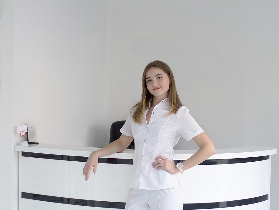 Female dental receptionist standing in front of the reception desk. 